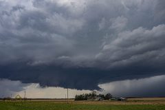 A dark, ominous severe thunderstorm with a dramatic lowering and wall cloud forming over the rural agricultural fields near Belleville, Kansas, on April 11, 2026. Extreme weather photography by storm chaser Mauro Greco