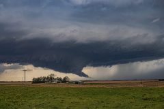 A dark, ominous severe thunderstorm with a dramatic lowering and wall cloud forming over the rural agricultural fields near Belleville, Kansas, on April 11, 2026. Extreme weather photography by storm chaser Mauro Greco