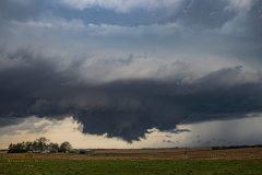 A dark, ominous severe thunderstorm with a dramatic lowering and wall cloud forming over the rural agricultural fields near Belleville, Kansas, on April 11, 2026. Extreme weather photography by storm chaser Mauro Greco